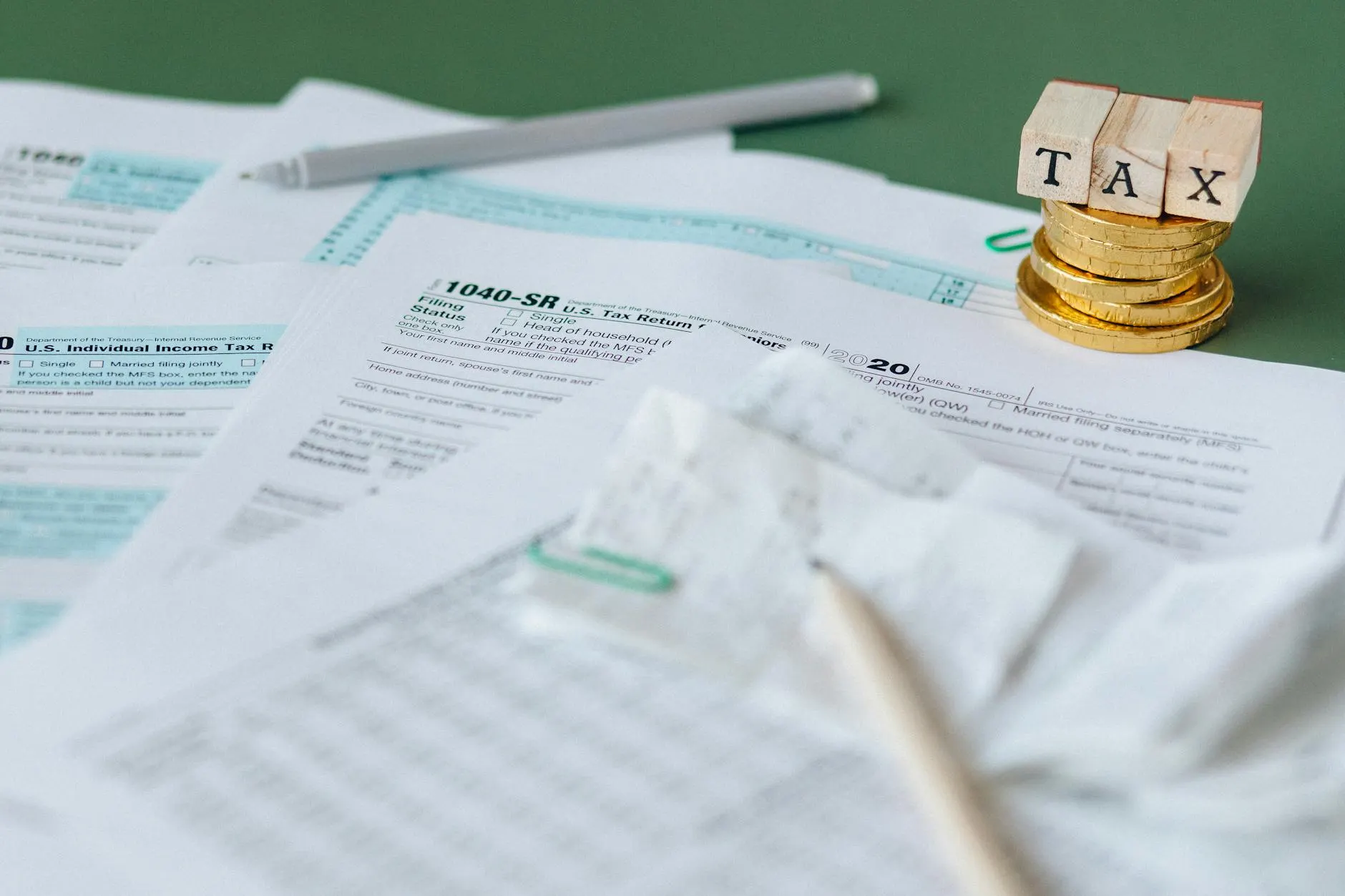 Detalhe de documentos fiscais e carimbos de impostos ao lado de pilhas de moedas e blocos com a palavra TAX, representando o que muda na prestação de serviços com a unificação dos impostos consumidos.