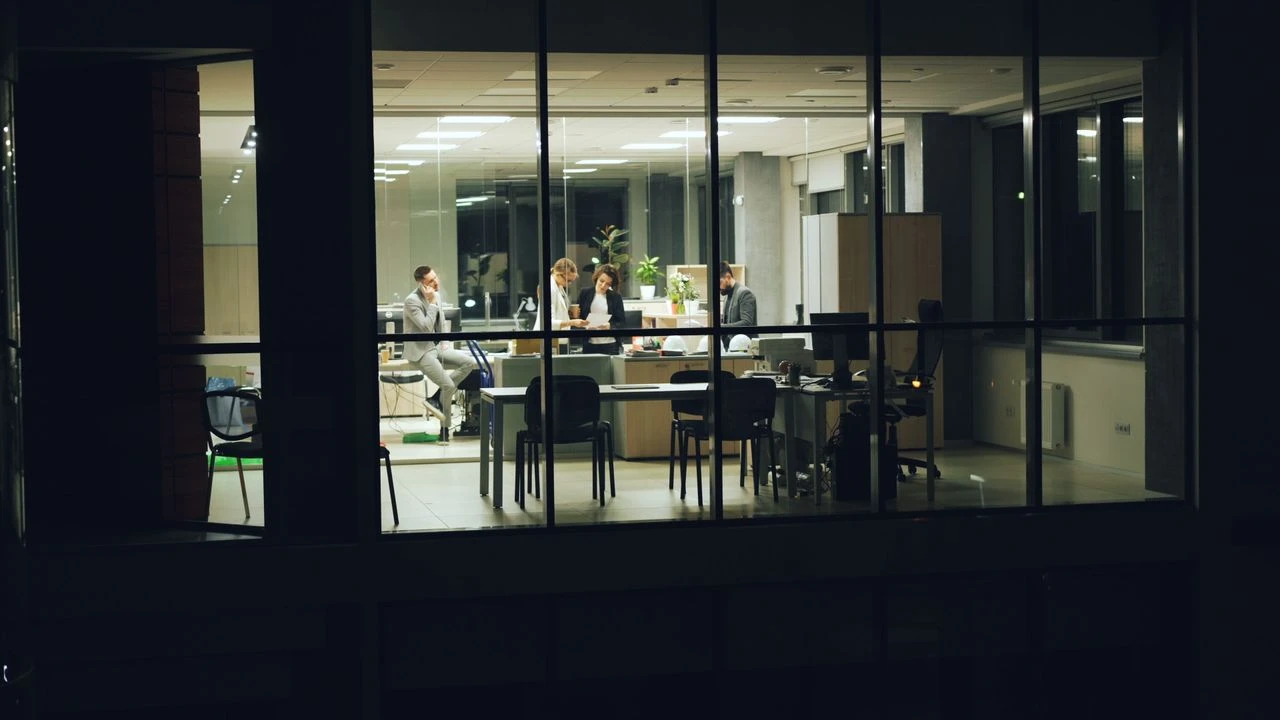 Equipe trabalhando em uma sala de reunião moderna com janelas de vidro, pessoas discutindo e analisando informações em ambiente corporativo iluminado, transmitindo foco e colaboração. Como melhorar a tomada de decisão no ambiente corporativo.